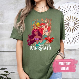 Puede incluir: Una camiseta verde con un estampado gr&aacute;fico de Ariel y una sirena negra de La Sirenita. El texto "The Little Mermaid" est&aacute; impreso debajo de la imagen.