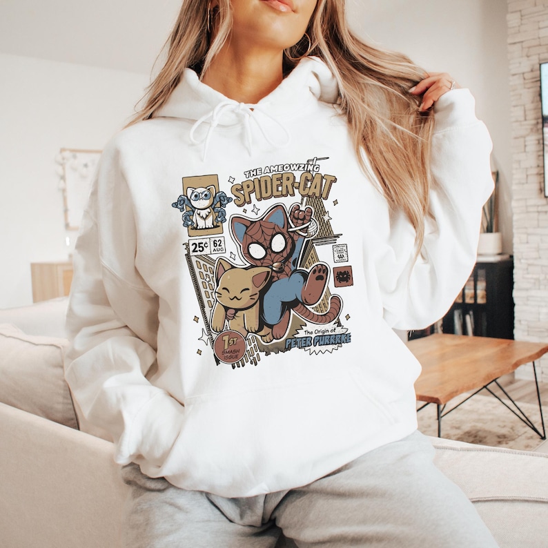 Puede incluir: Sudadera blanca con un estampado gr&aacute;fico de un gato de dibujos animados vestido de Spider-Man. El gr&aacute;fico incluye el texto "The Ameowzing Spider-Cat" y "The Origin of Peter Purrke".