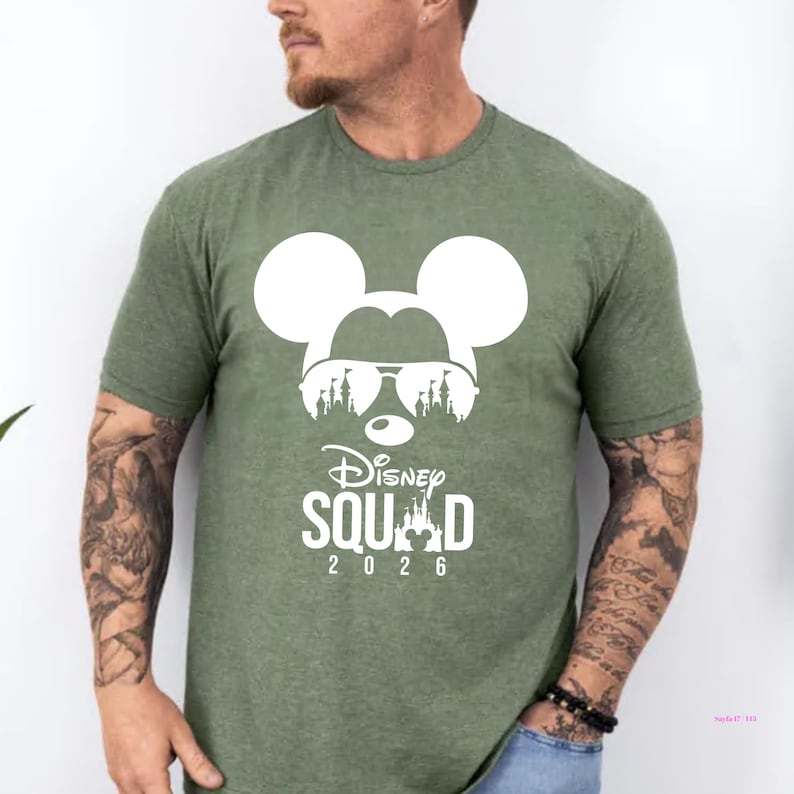 May include: Green t-shirt featuring a white graphic of Mickey Mouse wearing sunglasses, with a silhouette of a castle and the words "Disney Squad 2026". The shirt is made of a soft, comfortable material.