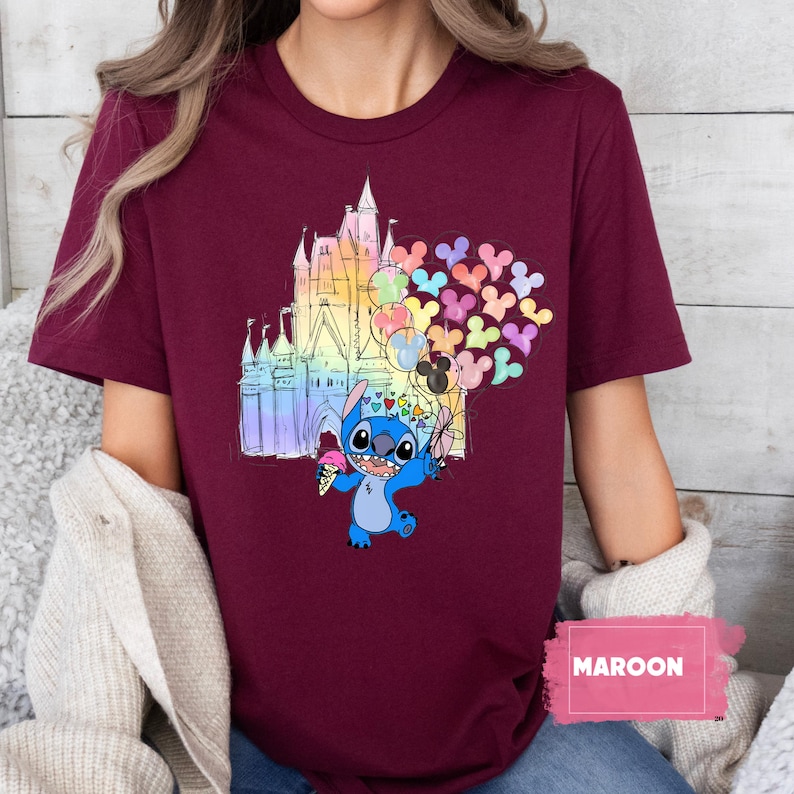 Puede incluir: Camiseta granate con un gr&aacute;fico colorido de un castillo, Stitch sosteniendo globos y un cono de helado. Los globos tienen forma de cabezas de Mickey Mouse. La palabra "MAROON" est&aacute; impresa en un rect&aacute;ngulo rosa.
