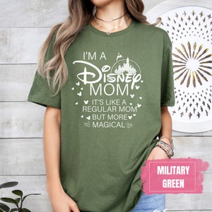 May include: Olive green t-shirt with the text "I'M A Disney MOM" in white, along with a castle graphic and Mickey Mouse icons. The shirt also says "It's like a regular mom but more magical."
