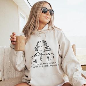 May include: A beige hoodie with a black and white illustration of William Shakespeare. The text on the hoodie reads "Stop making drama. You're not Shakespeare."