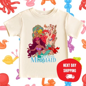 Puede incluir: Una camiseta blanca con un gr&aacute;fico de estilo vintage de Ariel y &Uacute;rsula de La Sirenita. El texto "The Little Mermaid" est&aacute; impreso debajo de la imagen.