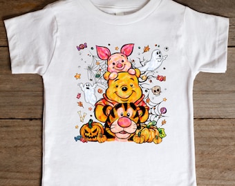 May include: White toddler t-shirt featuring a colorful Halloween-themed graphic. The design includes Winnie the Pooh, Piglet, and Tigger stacked together, surrounded by pumpkins, ghosts, spiderwebs, and candy. The shirt is made of a soft, comfortable material.