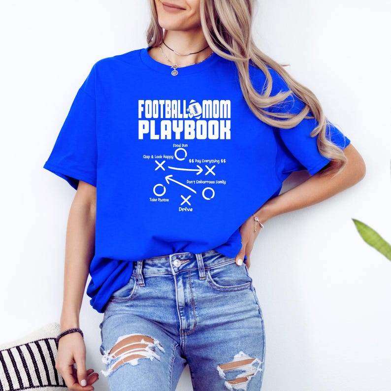May include: A royal blue t-shirt with a white graphic that says "Football Mom Playbook" and includes a football and a play diagram with the text "Gap & Lock Happy", "$$ Pay Everything $$", "Don't Embarrass Family", "Take Photos", and "Drive".