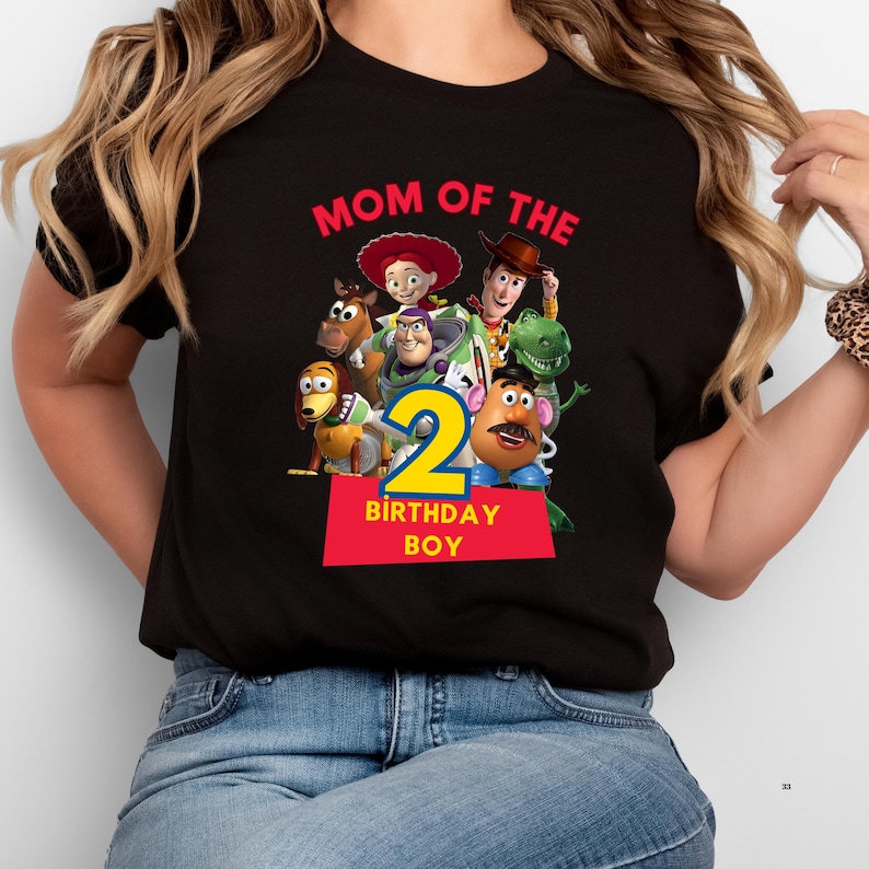 May include: Black t-shirt featuring a colorful graphic of characters from the Toy Story movie, with the text "MOM OF THE" above the characters and "2 BIRTHDAY BOY" below. The design includes Woody, Buzz Lightyear, and other characters.