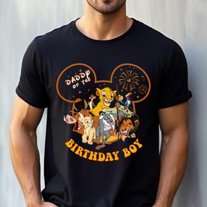 May include: Black t-shirt featuring a graphic of characters from The Lion King, including Simba, Timon, Pumbaa, and Scar. The design includes the text "Daddy of the Birthday Boy" in orange, set within a Mickey Mouse ear outline.