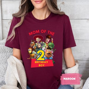 May include: Maroon t-shirt featuring a graphic of characters from the movie Toy Story. The design includes the text "MOM OF THE" above the characters and "2 BIRTHDAY BOY" below. The word "MAROON" is in a box at the bottom.