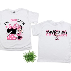 K&ouml;nnte beinhalten: Wei&szlig;e T-Shirts mit Minnie-Maus-Motiv. Ein Shirt zeigt den Text "Oh, Twoodles" mit einer rosa gepunkteten Zahl 2 und Minnie Maus. Das andere Shirt hat den Namen "Amelia" mit Minnie Maus.