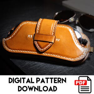 May include: A handcrafted, tan leather glasses case with white stitching and a secure strap closure. The case features embossed initials and holds sunglasses. The image includes the text "DIGITAL PATTERN DOWNLOAD" and a PDF icon.