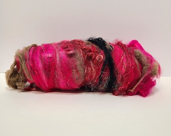 May include: A pink, brown, and black fiber blend yarn with a sparkly texture. The yarn is loosely wound and ready for knitting or crocheting.