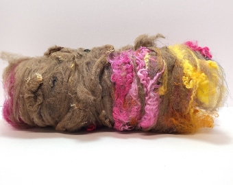 May include: A roll of brown, pink, and yellow wool roving. The roving is fluffy and textured, and it is perfect for spinning or felting.