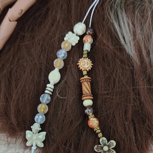 May include: Two beaded hair ties with white, brown, and gold beads. One hair tie has a butterfly charm and the other has a flower charm.
