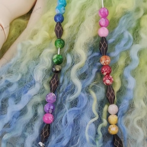 May include: Two beaded hair ties with wooden beads and colorful glass beads. One hair tie has a peace sign charm at the end and the other has a green and blue swirl charm.