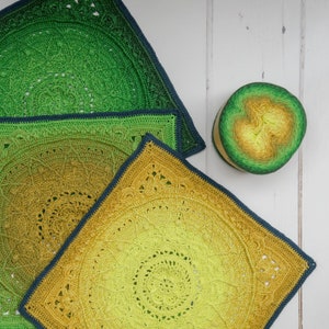 May include: Three crocheted squares in shades of green and yellow. The squares are layered on top of each other, with the largest square on the bottom and the smallest square on top. The squares are made with a circular pattern, and the colors gradually transition from green to yellow.
