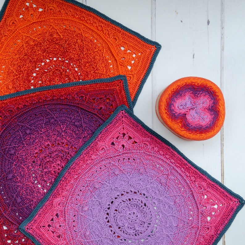 May include: Three crocheted squares in shades of orange, pink, and purple. The squares are layered on top of each other, with the largest square on the bottom and the smallest square on top. The squares are all made with a similar pattern, but the colors create a gradient effect.