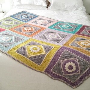 May include: A colorful crocheted throw blanket with a geometric pattern of squares and diamonds. The blanket features a floral design in the center of each square.