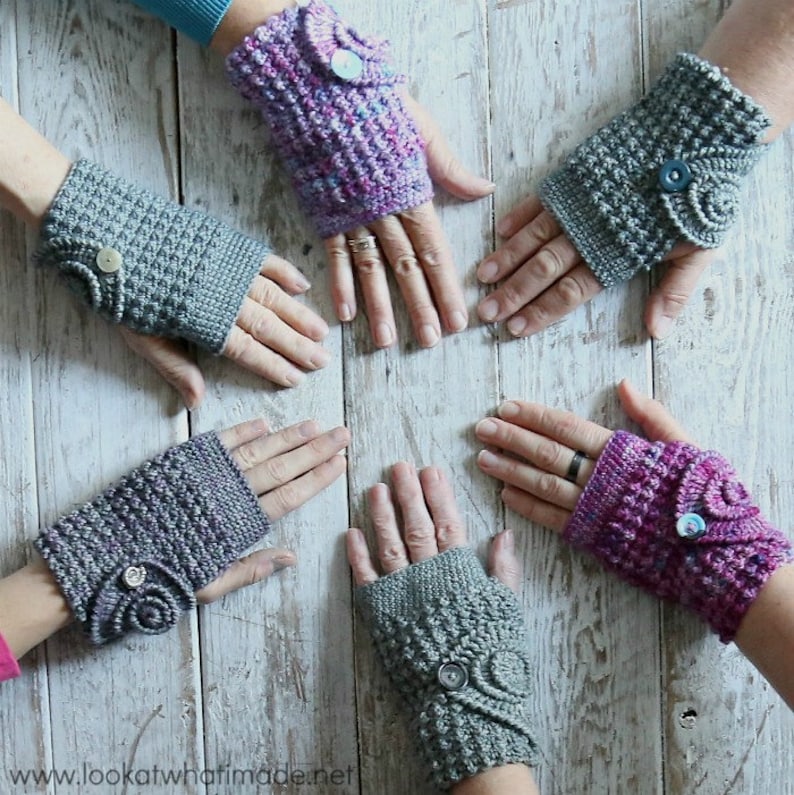 Op de afbeelding: Handgemaakte gehaakte vingerloze handschoenen in verschillende tinten grijs en paars. Elke handschoen heeft een knoop en een decoratief wervelontwerp. Gepresenteerd op een licht houten oppervlak.
