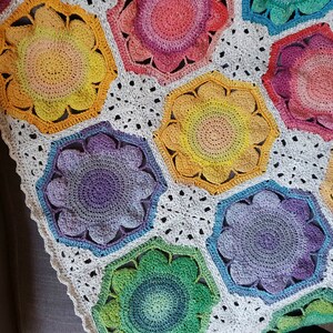 May include: A crocheted blanket with a hexagonal pattern featuring colorful flowers in shades of yellow, orange, red, purple, green, and blue.