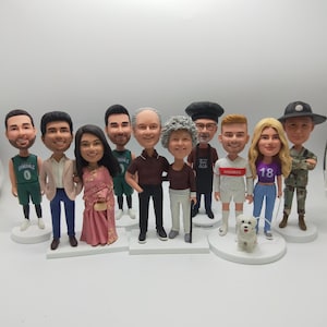 Op de afbeelding: Een verzameling gepersonaliseerde bobblehead-beeldjes, die elk een ander persoon in verschillende outfits uitbeelden. De beeldjes omvatten een basketballer, een persoon in een pak, een vrouw in een roze sari en een chef-kok.