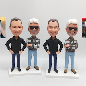 Op de afbeelding: Vier gepersonaliseerde bobbleheads van mannen in casual kleding. Elke bobblehead heeft een ander kapsel en gezichtskenmerken. De bobbleheads staan op een witte basis.