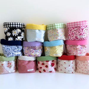 May include: A selection of fabric storage baskets in assorted sizes and patterns. The baskets display floral, gingham, and fruit designs in colours such as pink, white, red, and blue. Each basket has a contrasting fabric lining.