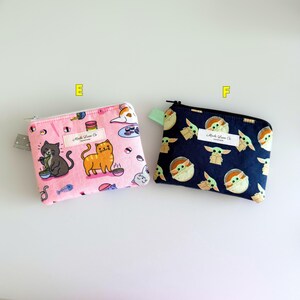May include: Two small zippered pouches with different designs. The pink pouch has a pattern of cats eating ramen and sushi. The blue pouch has a pattern of Baby Yoda characters. Both pouches have a white label with the text "Made Love Co."