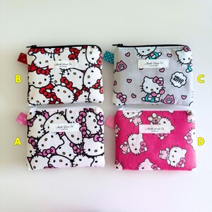 May include: Four small zippered pouches with Hello Kitty designs. The pouches are white with pink and black Hello Kitty characters. The pouches are lined up in a row from left to right. The pouches are made by Mache Lane Co. The pouches are handmade.