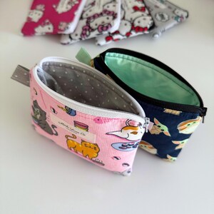 May include: Two zippered pouches, one pink with a cat and sushi design and the text "Mocha Llama Co." and the other navy blue with a green alien design.
