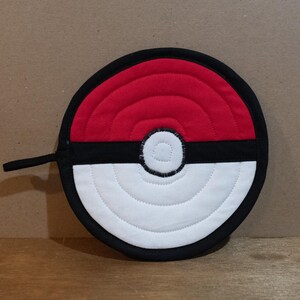 May include: A red, white, and black quilted hot pad shaped like a Pokeball. The hot pad has a black handle.