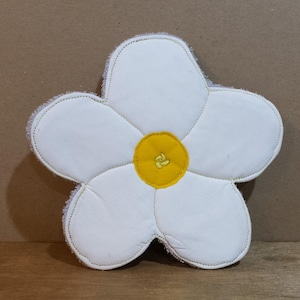 May include: White flower-shaped pot holder with a yellow centre. The pot holder is made of a soft, textured fabric.