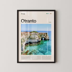 Puede incluir: Un póster enmarcado con un paisaje costero de Otranto, Italia. La imagen muestra acantilados blancos, agua turquesa y un cielo azul. La palabra "Otranto" está impresa en negrita en la parte superior, con "Italia" debajo. El póster está en un marco negro.