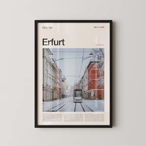 May include: Framed poster featuring a snowy street scene in Erfurt, Germany. The image shows a tram on tracks, flanked by buildings. The poster includes the city name "Erfurt" and the country code "DEU".