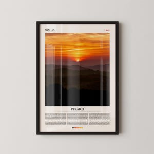 May include: Framed print featuring a vibrant sunset over rolling hills. The sky is ablaze with orange and yellow hues, with the sun setting in the distance. The print includes the text "PESARO" and "/ Italy".