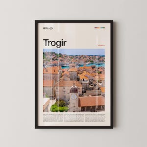 Puede incluir: Póster enmarcado con una vista panorámica de Trogir, Croacia, con una torre del reloj y tejados de tejas rojas. El póster incluye el texto "Trogir" y "/ croatia" en un diseño minimalista, con un fondo color crema.