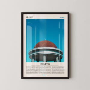 Puede incluir: Lámina artística enmarcada con una fotografía de un edificio en Donetsk, Ucrania. El edificio tiene una cúpula roja y columnas blancas, sobre un cielo azul brillante. La palabra "DONETSK" está impresa debajo.