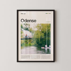 May include: Framed poster featuring the word "Odense" above a scenic photo of a river with a bridge and a cyclist. The image includes text that reads "/ denmark" and additional text at the bottom. The frame is black.