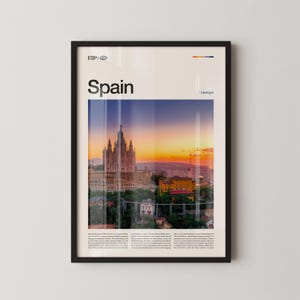 May include: Framed poster featuring a scenic view of a Spanish city at sunset. The word "Spain" is printed in large, bold letters at the top. The image includes a tall building with a distinctive architectural style.