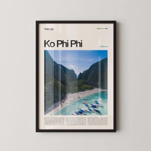 May include: Framed poster featuring a scenic aerial view of Ko Phi Phi, Thailand. The image showcases a white sandy beach, turquoise water, and lush green mountains. The poster includes the text "Ko Phi Phi" and "Thailand".