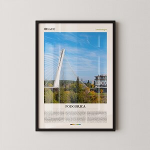 Puede incluir: Impresión enmarcada que presenta un puente blanco moderno contra un cielo azul. La imagen incluye el texto "PODGORICA" y otro texto en la parte inferior. La impresión está en un marco negro y se muestra en una pared blanca.