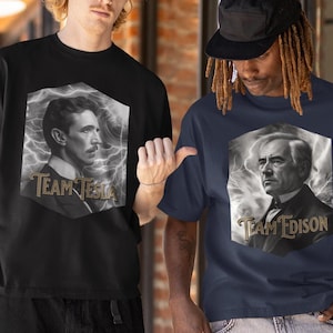 Puede incluir: Dos personas con camisetas negras y azul marino con imágenes de Nikola Tesla y Thomas Edison. Las camisetas tienen el texto "Team Tesla" y "Team Edison" impreso.