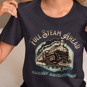 May include: A dark grey t-shirt featuring a vintage-style illustration of a steam train. The text "Full Steam Ahead Railway Adventures!" is printed on the shirt.