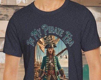 Könnte beinhalten: Ein marineblaues T-Shirt mit einem Grafikdruck eines Piratenkapitäns, der auf dem Deck eines Schiffes steht. Der Text "In My Pirate Era" ist in einem Kreisbogen um das Bild geschrieben.