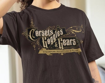 May include: A person wearing a brown t-shirt with a gold graphic that says "Corsets, Goggles & Gears" and the text "Steampunk Adventure is Near!"