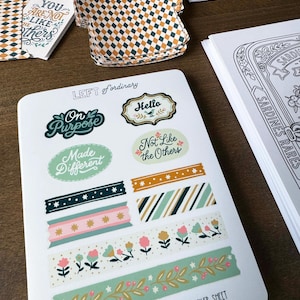 May include: A sheet of vinyl stickers with various designs, including phrases like "On Purpose" and "Not Like the Others." The sheet also features decorative tape designs with floral and geometric patterns. The text "MAJESTIC CRUMBS STUDIO" and "VINYL STICKER SHEET" are visible.