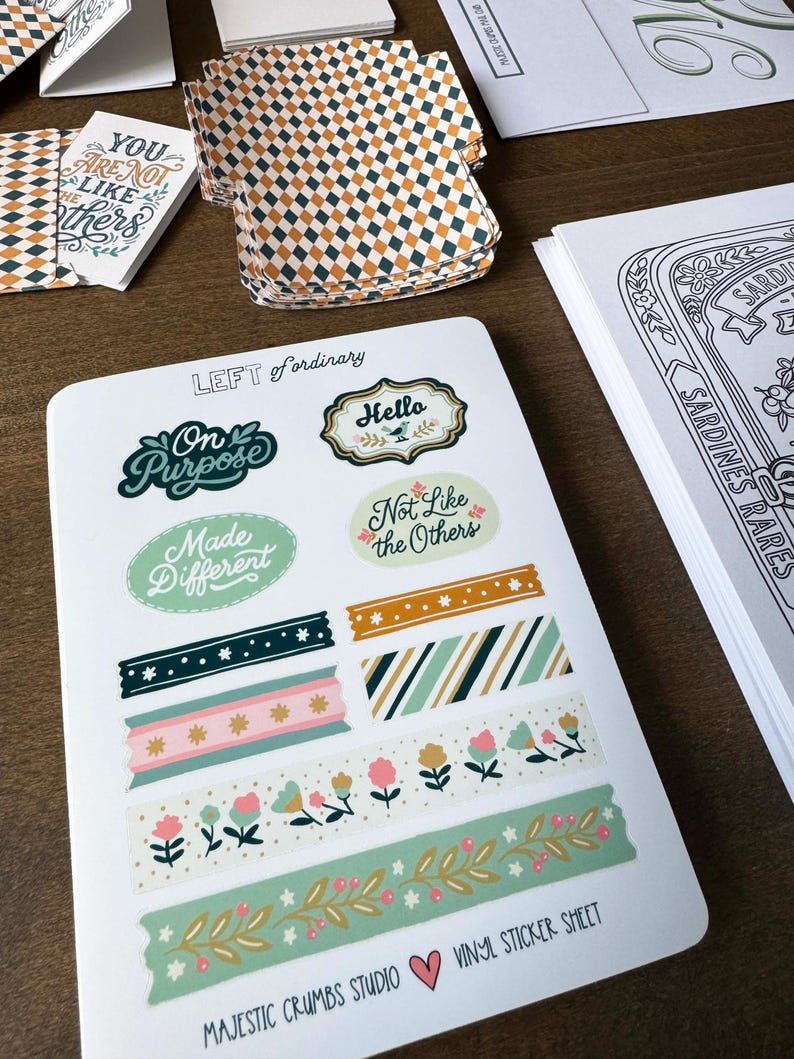May include: A sheet of vinyl stickers with various designs, including phrases like "On Purpose" and "Not Like the Others." The sheet also features decorative tape designs with floral and geometric patterns. The text "MAJESTIC CRUMBS STUDIO" and "VINYL STICKER SHEET" are visible.