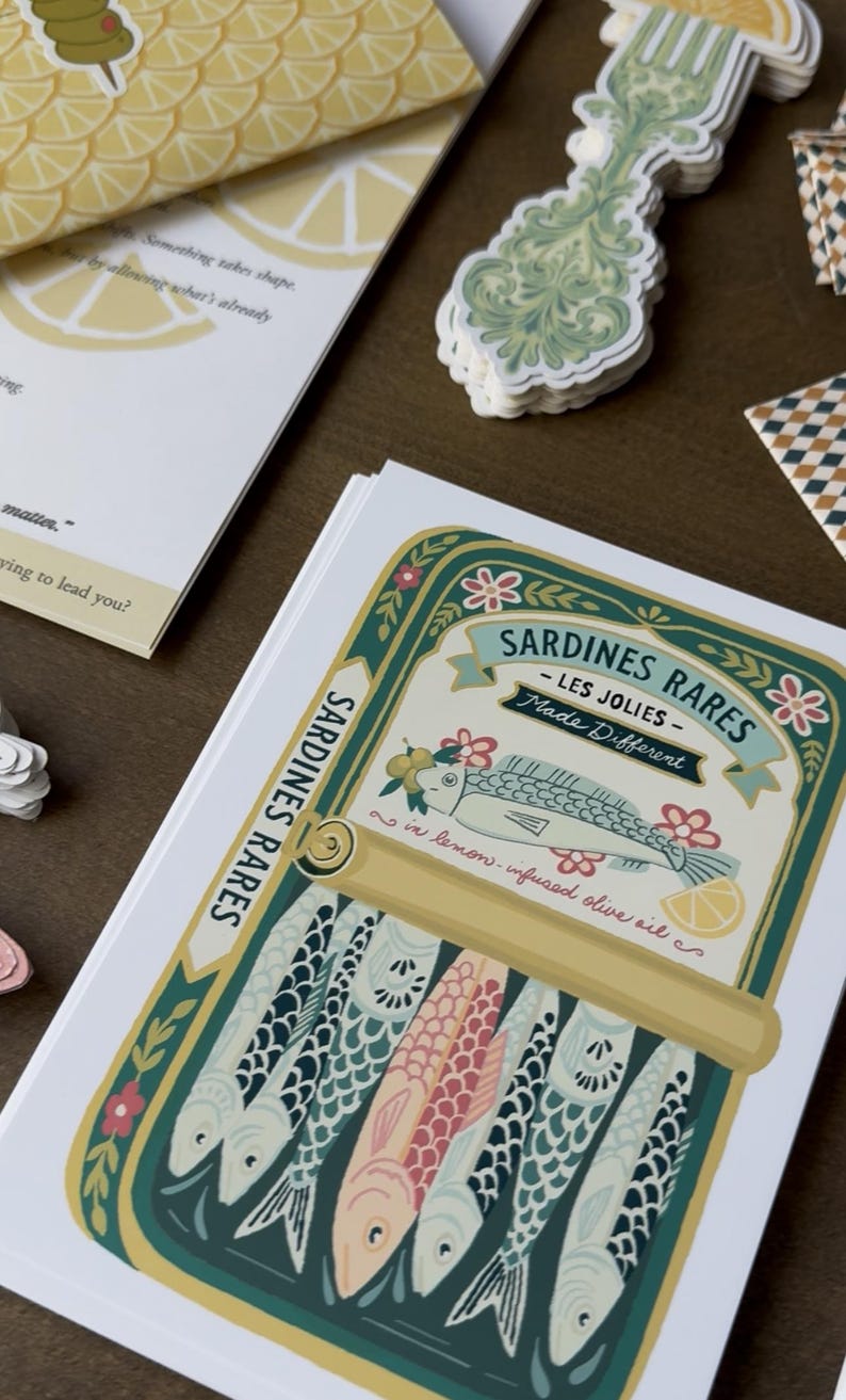 May include: A stack of paper goods featuring a sardine can illustration with the text "Sardines Rares - Les Jolies - Made Different". The can design includes fish, flowers, and lemon slices. Other items include a lemon-patterned card and decorative stickers.