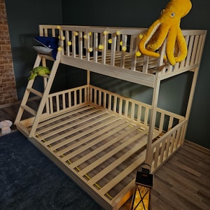 Puede incluir: Una litera de madera con una escalera y un caj&oacute;n incorporado. La cama est&aacute; hecha de madera natural y tiene un dise&ntilde;o sencillo. La litera superior tiene un juguete de peluche de pulpo amarillo y una cadena de luces blancas. La litera inferior tiene un juguete de peluche de ballena azul.
