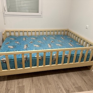 May include: A light wood crib with a blue and white patterned sheet. The crib has a high wooden railing around the perimeter.