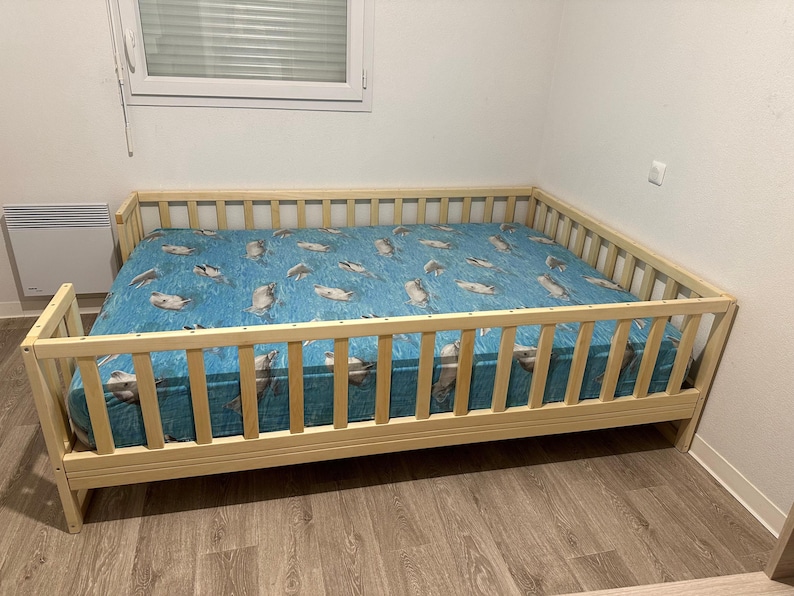 May include: A light wood crib with a blue and white patterned sheet. The crib has a high wooden railing around the perimeter.